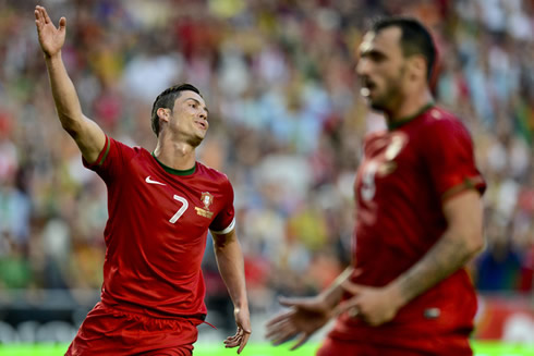 Cristiano Ronaldo waving and stretching his right arm in a game for Portugal, while Hugo Almeida looks ahead