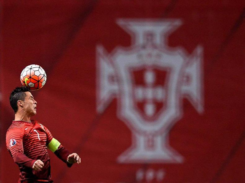 Cristiano Ronaldo heads a ball with a Portuguese banner in the background