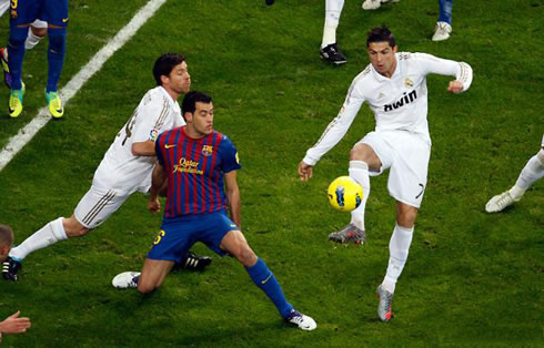 Cristiano Ronaldo about to touch the ball in Real Madrid vs Barcelona, while Xabi Alonso pushes Busquets
