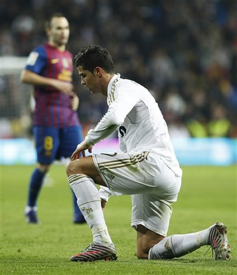 Cristiano Ronaldo with a knee on the ground in a game between Real Madrid and Barcelona, while Iniesta stands near him