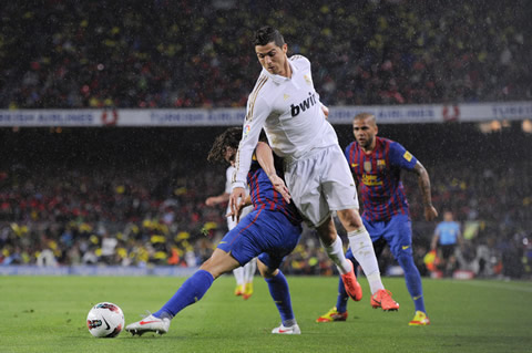 Cristiano Ronaldo trying to reach the ball, while Carles Puyol protects it with the body