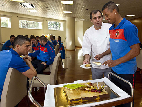 Cristiano Ronaldo looking at Nani taking a slice of cake, near Hélio Loureiro