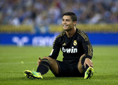Cristiano Ronaldo tersenyum, duduk dengan di lapangan dengan kaki terbuka 
