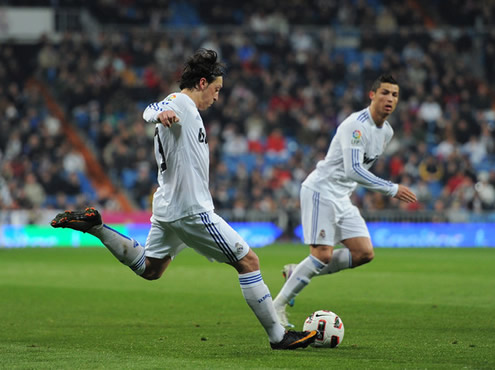 Mesut Ozil shooting the ball, with Cristiano Ronaldo near him and starting to run