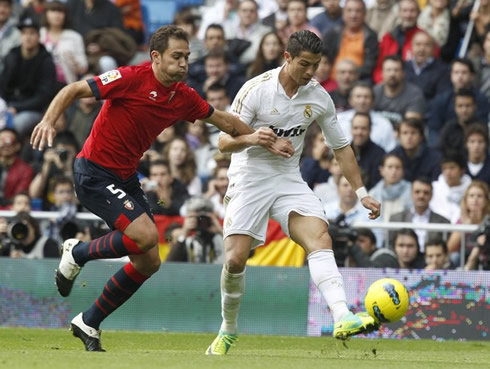 Cristiano Ronaldo strikes the ball with his left foot while being pushed by a Osasuna defender