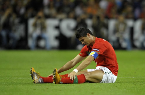 Cristiano Ronaldo sits on the ground with his legs stretched and visibly in pain