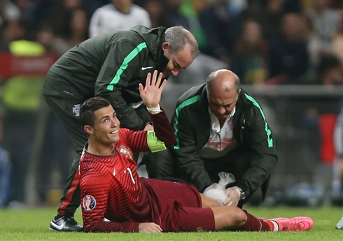 Cristiano Ronaldo smiling and showing his hand to the referee, as he gets assisted by the Portuguese medical doctors
