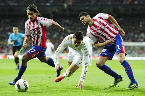 Cristiano Ronaldo being sent down in between two Sporting Gijon defenders, in 2012