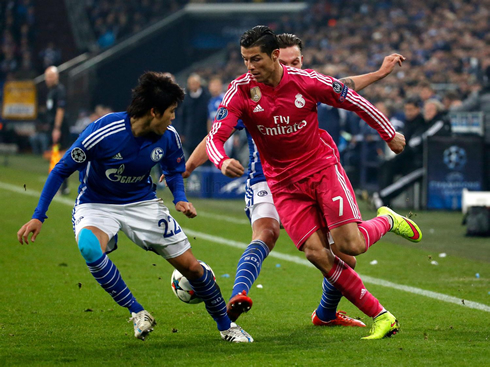 Cristiano Ronaldo dribbling right between two defenders, in a UEFA Champions League night game between Schalke and Real Madrid