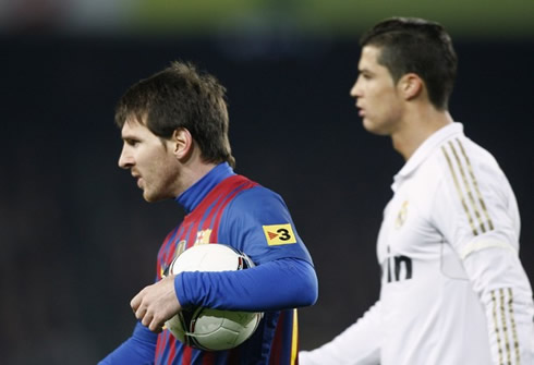 Lionel Messi holding to the ball, with Cristiano Ronaldo walking near him in a Barcelona vs Real Madrid Clasico, in 2012