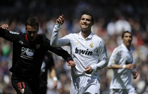 Cristiano Ronaldo smiles and raises his hand while a Sevilla players still looks at the ball