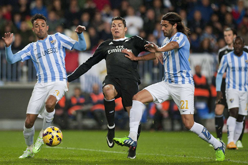 Cristiano Ronaldo stretching in order to try reaching to the ball before two Malaga players