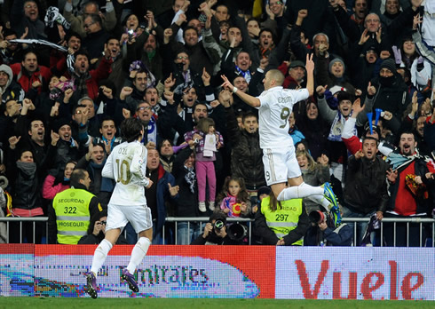 Benzema jumping in the air, while celebrating a goal for Real Madrid, with Ozil near him and the crowd going wild