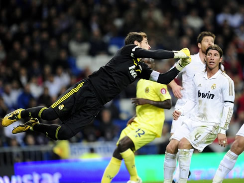 Iker Casillas flying to reach the ball, while Sergio Ramos and Xavi Alonso follow up, in a Real Madrid game in 2011-2012