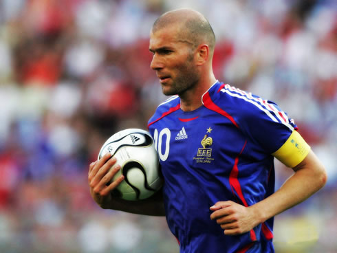 Zinedine Zidane in a France blue classic shirt/jersey, being the team captain and running with the ball under his arm