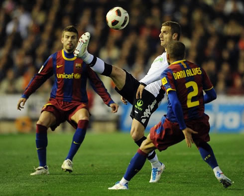 Roberto Soldado controlling the ball, while defended by Daniel Alves and Gerard Piqué, in Valencia vs Barcelona in 2012