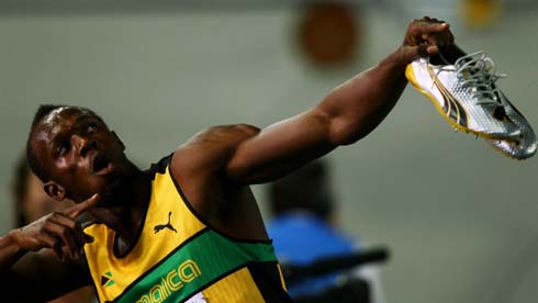 Usain Bolt doing the bolt gesture, while holding his running shoes