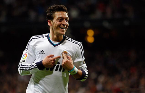 Mesut Ozil pointing to Real Madrid badge and symbol, as he celebrates a goal against Atletico Madrid, in 2012-2013