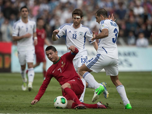Cristiano Ronaldo on the ground, fighting for the ball against two opponents from Israel, in 2013