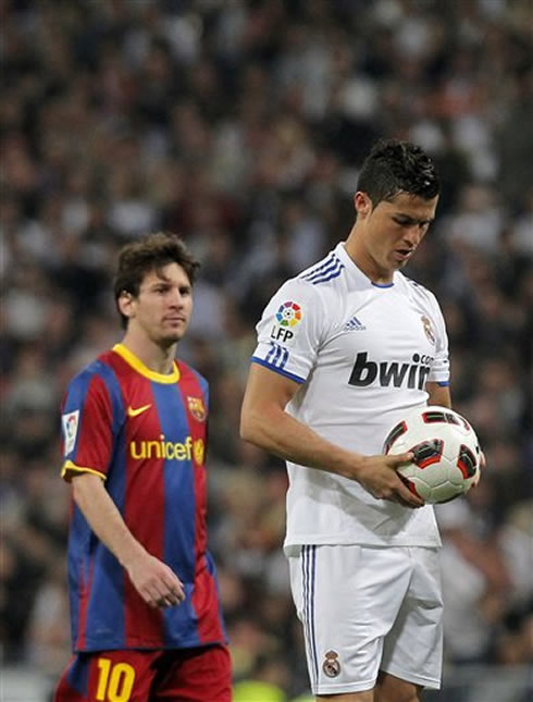 Cristiano Ronaldo holding the ball before taking a penalty kick, with Messi starring right behind him