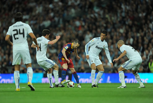 Iniesta protecting the ball while being surrounded by Real Madrid players, including Cristiano Ronaldo